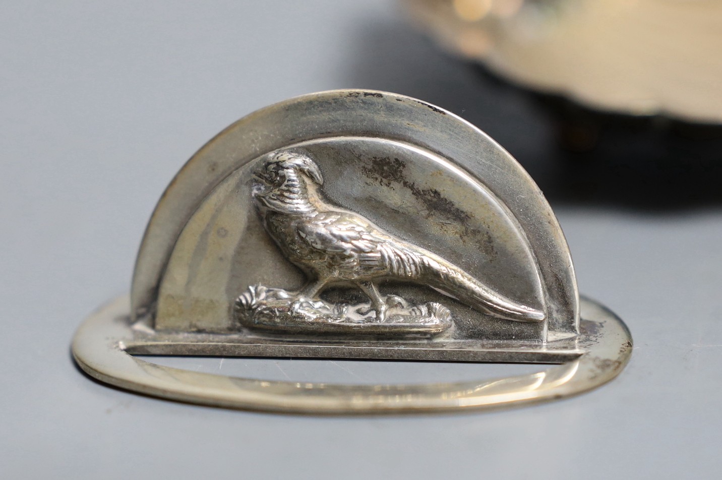 A pair of silver menu card holders, each decorated with a pheasant, Sampson Mordan & Co, Chester, 1907, width 59mm and a silver butter shell.